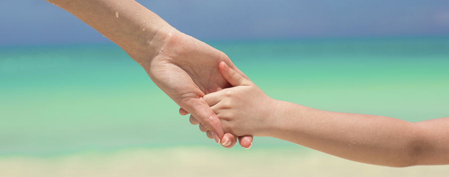 Close-up hands of mother and little kid walking on the beach