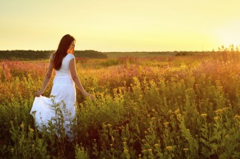 Young woman in white clothes standing in field on sunset